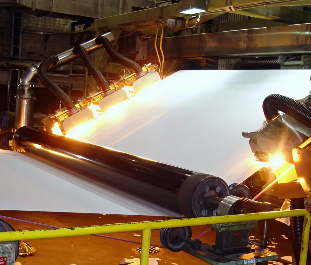 Industrial infrared dryers heating a moving paper sheet on rollers in a production line.