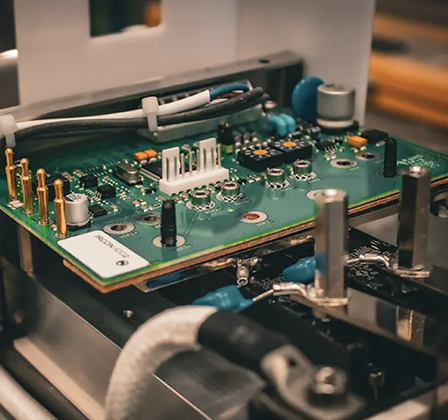 Close-up view of an electronic circuit board with visible components, connectors, and wiring inside a metal enclosure.