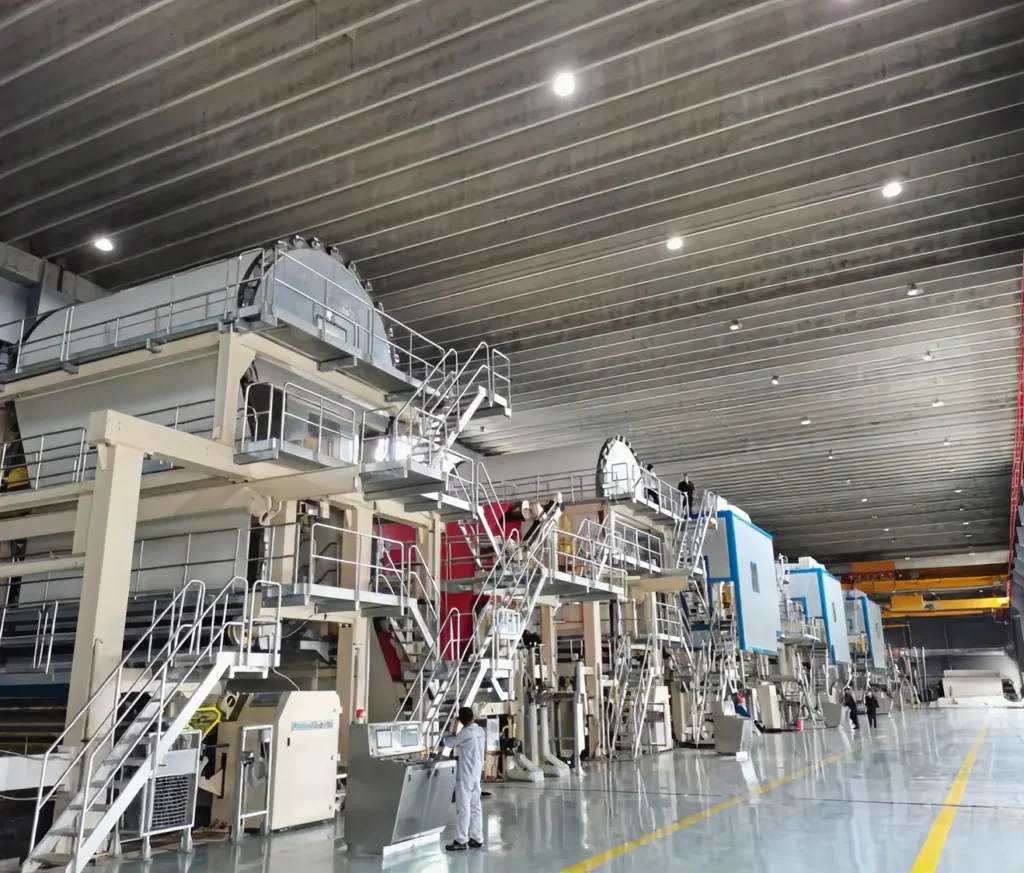 Large industrial paper machine with metal platforms and workers inside a factory.